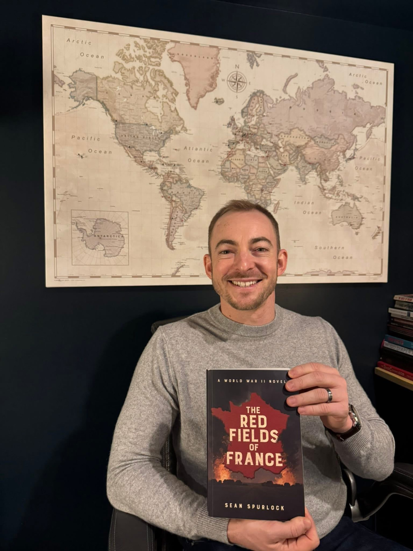Sean Spurlock holding The Red Fields of France in front of a vintage world map
